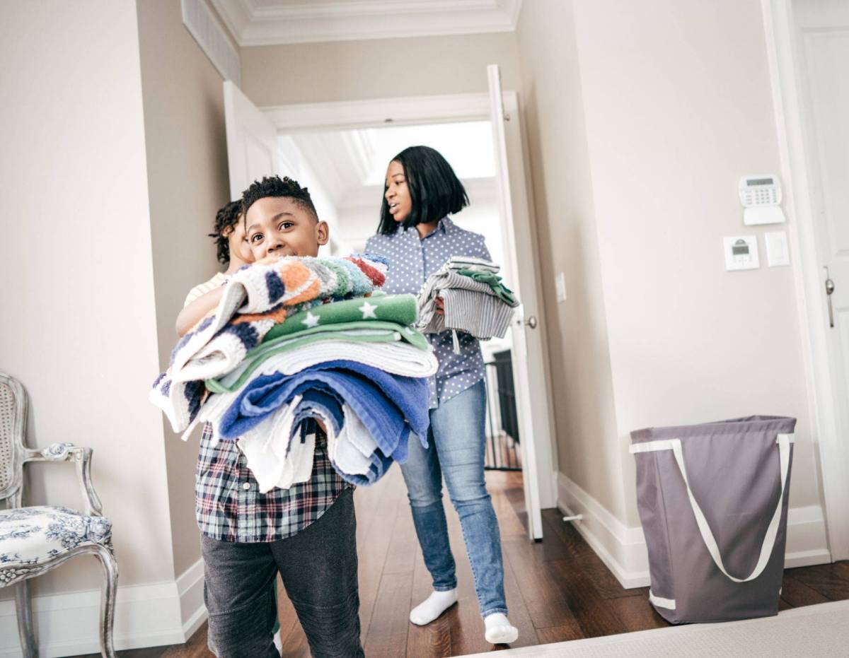 Three young family members carry freshly folded towels in their home.